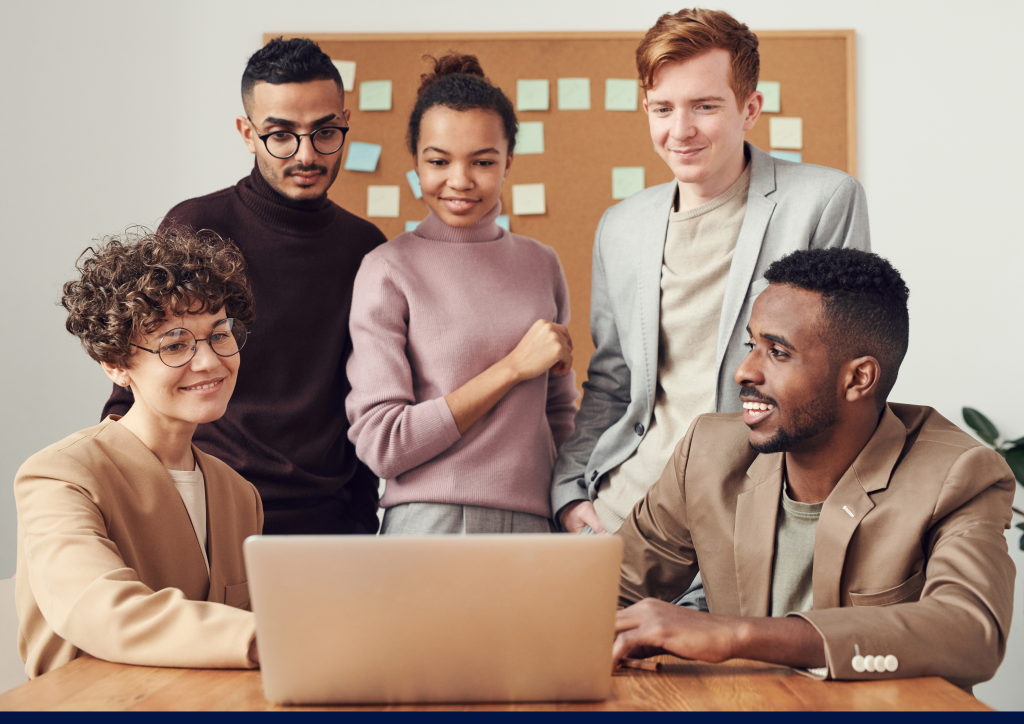 A group of people in office seeing on screen while person siting on chair with laptop on desk explaining people about guidane of server